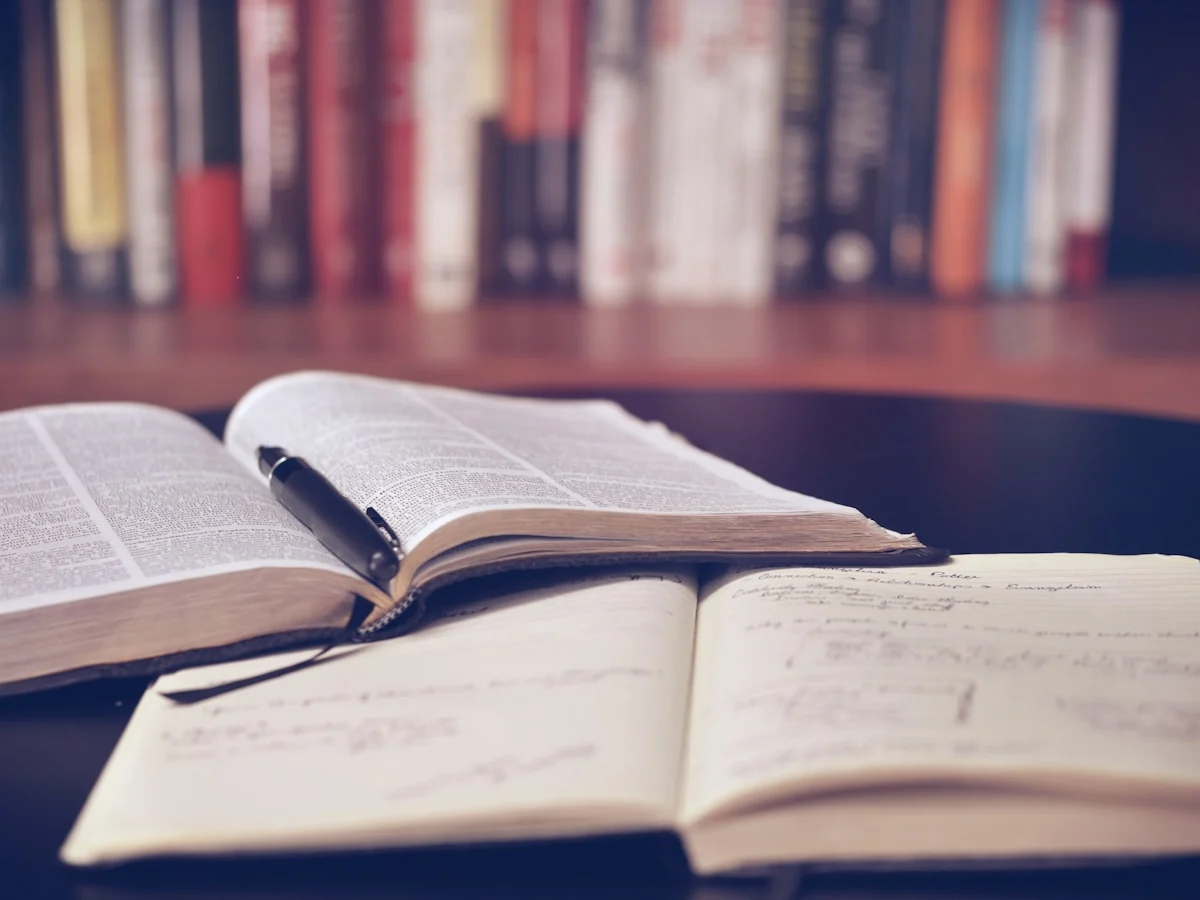An open book and coffee on a wooden table by a window